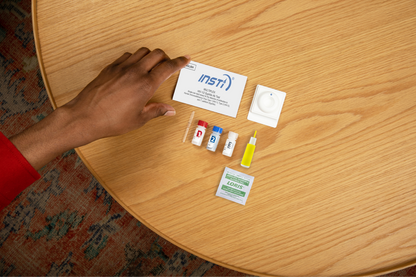 INSTI Multiplex HIV1/2 Syphilis Ab Test contents including reagent bottles, lancet, and instructions on table