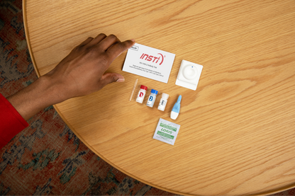 INSTI HIV-1/HIV-2 Antibody Test contents including reagent bottles, lancet, and instructions on table
