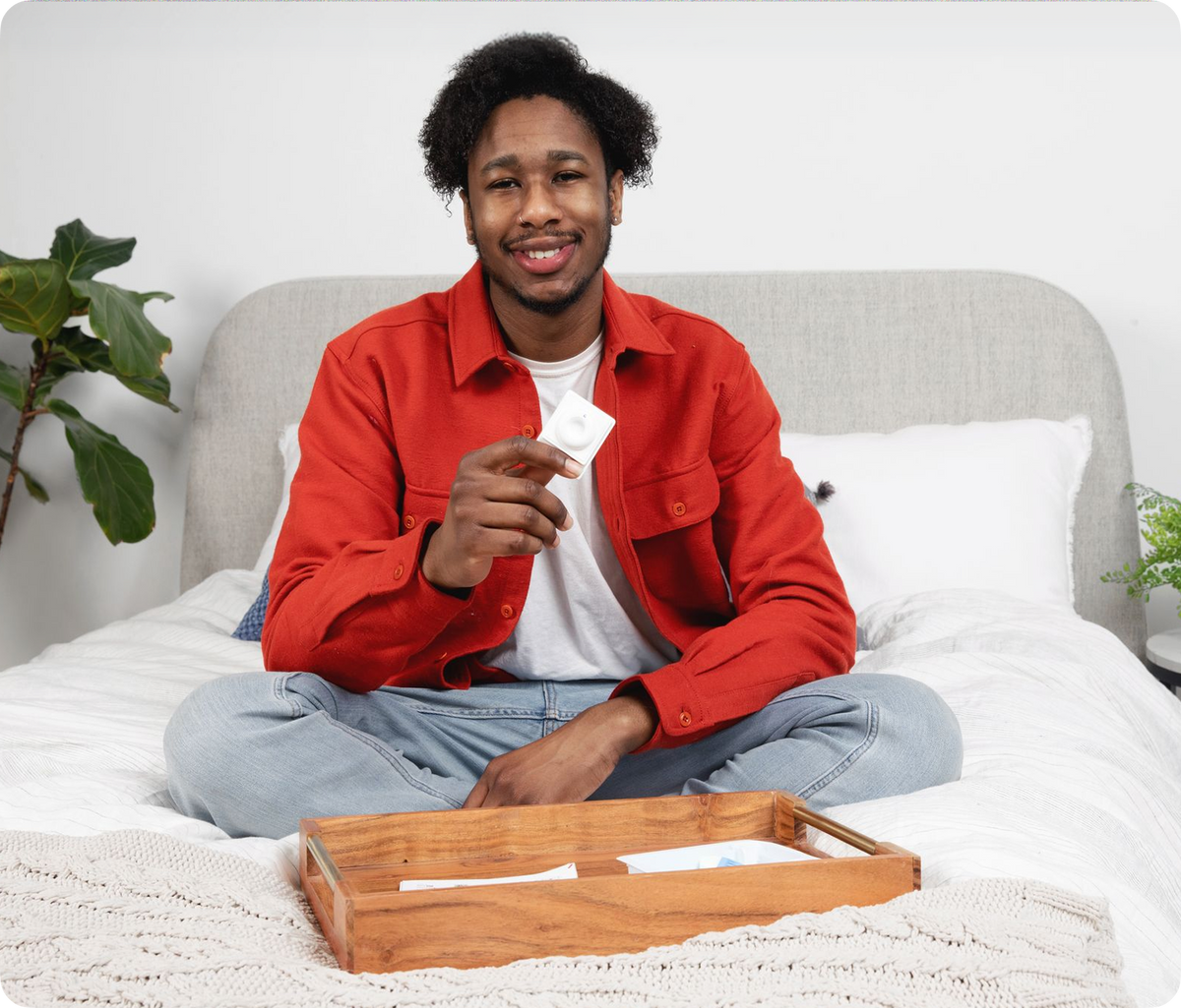 Man sitting on bed holding INSTI HIV self-test device after completing home HIV test